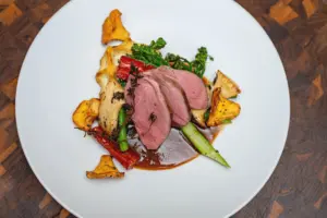 Hauptgang mit rosa gebratener Ente, Pfifferlingen und Gemüse auf weißem Teller – Foodfotografie Restaurant