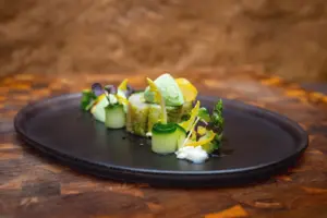 Vorspeise mit Gurke, Kräutern und Blüten auf dunklem Teller – Foodfotografie für ein Restaurant