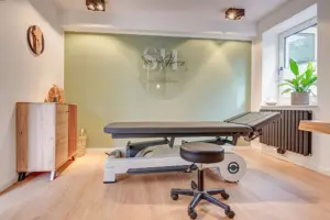 Heller Behandlungsraum einer Osteopathie-Praxis mit Therapieliege und salbeigrüner Wand