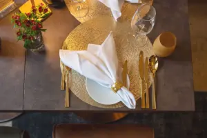 Eingedeckter Restauranttisch von oben mit goldenem Besteck, Platzset und weißer Serviette