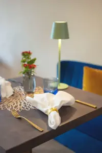 Restauranttisch mit grüner Tischleuchte, blauer Sitzbank und goldenem Besteck